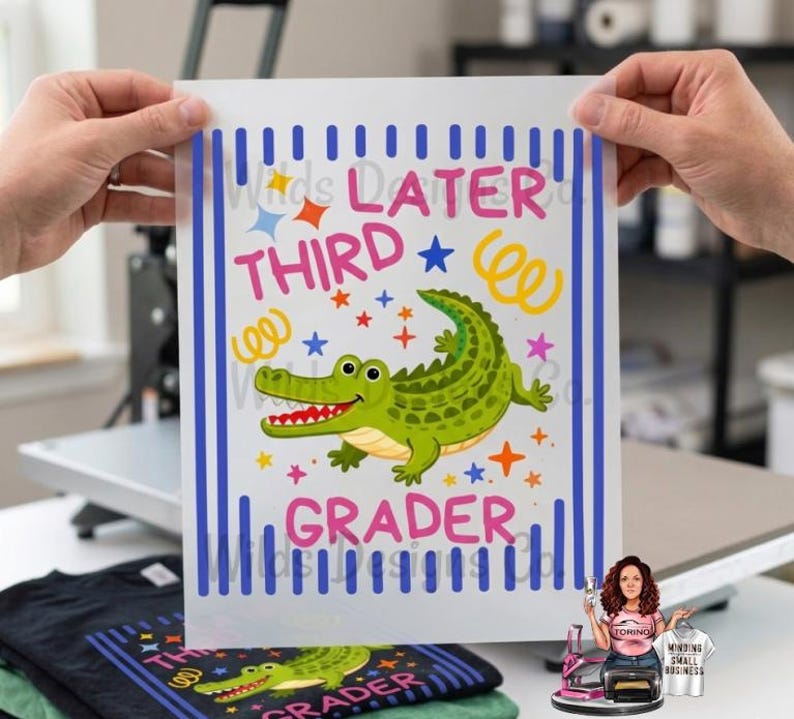 Pu&ograve; includere: Un foglio di trasferimento a sublimazione bianco con la scritta "Later Third Grader" e un alligatore dei cartoni animati. Il disegno include strisce verticali blu, stelle e coriandoli. Il foglio &egrave; tenuto in mano.