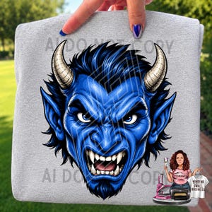 Op de afbeelding: Een grijs gemêleerd t-shirt met een grote, gedetailleerde afbeelding van een blauwhuidig wezen met scherpe witte hoektanden, puntige oren en twee gekromde hoorns. Het wezen heeft een intense, grommende uitdrukking met donkerblauw haar.
