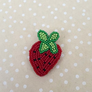 May include: A red and green beaded strawberry brooch. The strawberry is made of small red beads and has a green beaded leaf on top.