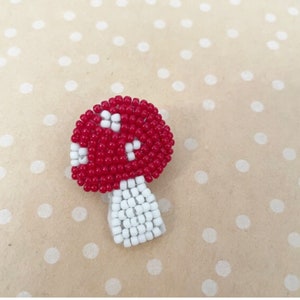 May include: A red and white beaded mushroom with a white stem. The mushroom is made of small beads and has a rounded top.