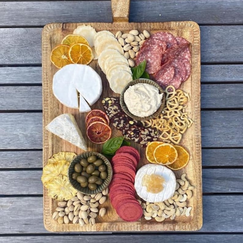 May include: A wooden serving board with a selection of snacks, including cheese, salami, dried fruit, nuts, and crackers.