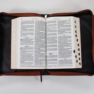 May include: A brown leather-bound Bible with a zipper closure and a black interior. The Bible is open to Psalms 117 and 118.