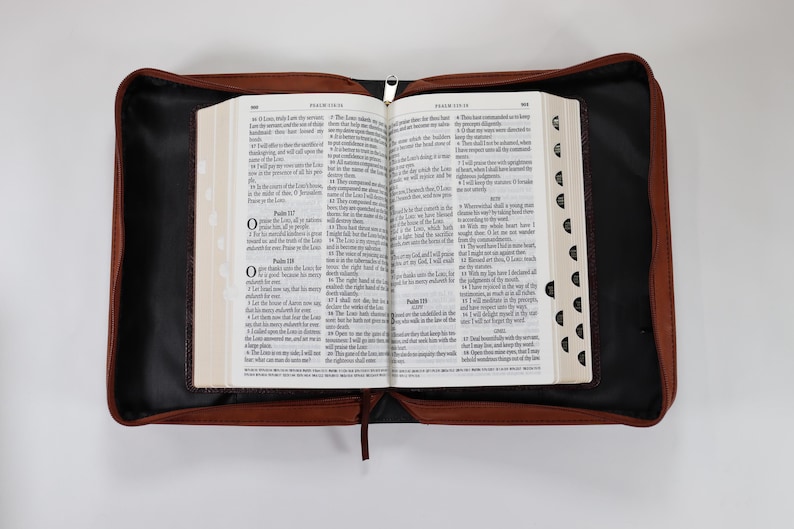 May include: A brown leather-bound Bible with a zipper closure and a black interior. The Bible is open to Psalms 117 and 118.