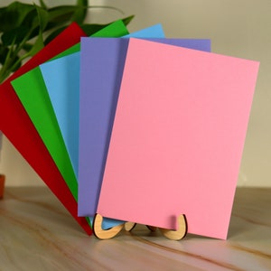 May include: A set of five blank cards in different colors, red, green, blue, purple, and pink, standing upright in a wooden card holder.