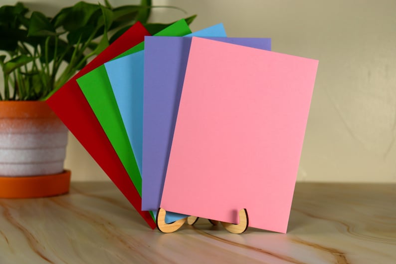 May include: A set of five blank cards in different colors, red, green, blue, purple, and pink, standing upright in a wooden card holder.