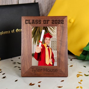 May include: A wooden picture frame with a graduation photo inside. The frame is engraved with "Class of 2022", "Tyler House", and "Carson University".