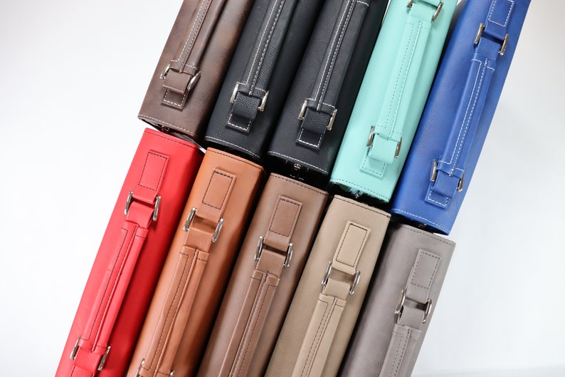 May include: A stack of ten different coloured leather zippered cases with silver buckles and handles.