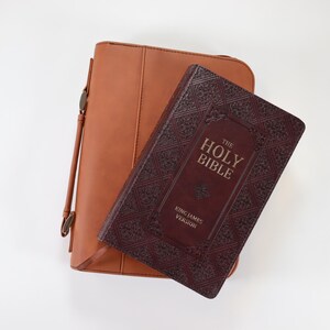 May include: A brown leather Bible cover with a burgundy Bible inside. The Bible has gold lettering that reads "The Holy Bible King James Version".