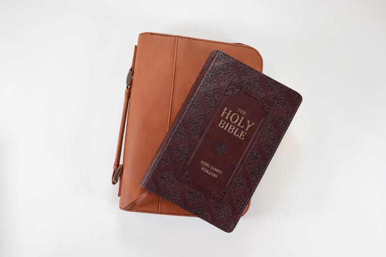 May include: A brown leather Bible cover with a burgundy Bible inside. The Bible has gold lettering that reads "The Holy Bible King James Version".