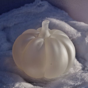 May include: A white frosted glass pumpkin shaped decorative object sitting on a white fluffy surface.