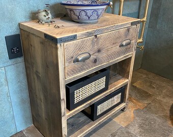 May include: Rustic wooden bathroom vanity with a single drawer, two open shelves, and a black metal drawer pull. The vanity has a white ceramic sink with a blue and white patterned design. The vanity is sitting on a tiled floor.