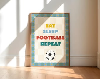 May include: A framed print with the words "EAT SLEEP FOOTBALL REPEAT" in yellow, blue, red, and green. A soccer ball graphic is at the bottom. The print has a light wood frame and is set against a white wall and wooden floor.