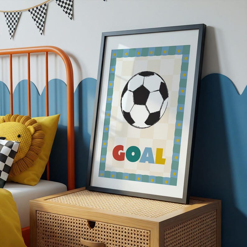 May include: Framed soccer-themed art print featuring a black and white soccer ball illustration. The word "GOAL" is displayed in colorful letters below the ball. The print has a blue and yellow border and is set against a checkered background.