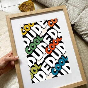 May include: A framed print with the word "COOL DUDE" in a repeating pattern. The word "COOL" is in yellow, green, orange, and blue. The frame is light brown.