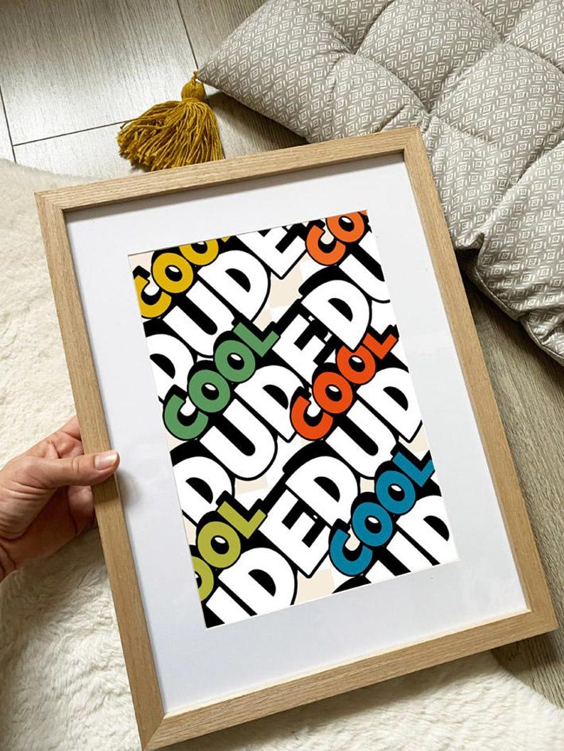 May include: A framed print with the word "COOL DUDE" in a repeating pattern. The word "COOL" is in yellow, green, orange, and blue. The frame is light brown.