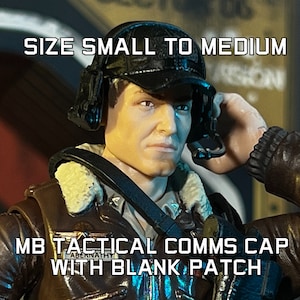Puede incluir: Una gorra de comunicaciones tácticas MB negra con un parche en blanco, talla pequeña a mediana, se muestra en una figura. La gorra tiene orejeras y un aspecto de cuero. La figura lleva una chaqueta de aviador marrón.