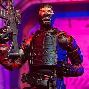 Può includere: Action figure di un soldato in equipaggiamento tattico, con un fucile nero. La figura indossa un passamontagna nero, un giubbotto tattico e maniche mimetiche. Lo sfondo è un mix di viola e blu.