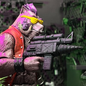 May include: A brown anthropomorphic boar action figure with a purple mohawk, wearing yellow sunglasses and a red vest. The figure holds a dark gray rifle with a scope and a drill-like barrel attachment, featuring a black studded wristband.