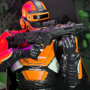 Op de afbeelding: Een sciencefiction-actiefiguur met een feloranje en zwarte helm met een donker vizier en bijpassende oranje en zwarte bepantsering. Het figuur houdt een gedetailleerd zwart geweer met een vizier vast en heeft zichtbare gewrichtsverbindingen.