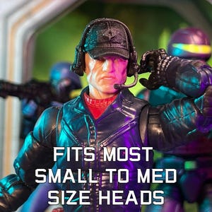 Puede incluir: Figura de acción de un hombre con gorra negra, auriculares y micrófono. La figura lleva una chaqueta negra sobre una camisa roja. El texto "FITS MOST SMALL TO MED SIZE HEADS" se muestra en letras blancas.