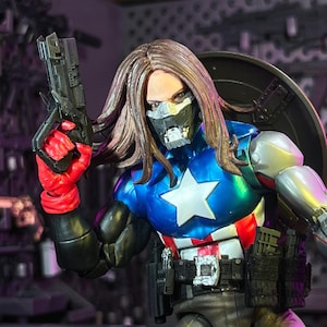 May include: A detailed action figure featuring long brown hair, a metallic silver face mask, and a blue chest piece with a white star. The figure wears red gloves, holds a black pistol, and has a silver robotic arm with a shield on the back.