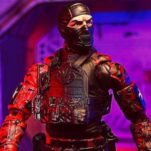 Puede incluir: Figura de acción de un personaje con un traje táctico negro con máscara y casco negros. La figura tiene detalles de camuflaje rojo y negro en brazos y piernas. El pecho presenta un chaleco negro con un emblema plateado.