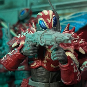 Peut inclure: Figurine d'action rouge et blanche avec un casque et une armure détaillés, tenant une arme grise. La figurine a des yeux bleus et des motifs complexes sur son armure. Le thème général suggère un personnage de science-fiction ou fantastique.