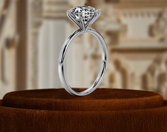 May include: A simple solitaire engagement ring with a round brilliant cut diamond set in a four-prong setting. The ring is made of white gold and has a thin band.