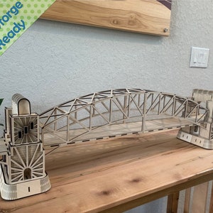 Könnte beinhalten: Ein Holzmodell einer Brücke mit filigranen Details. Die Brücke besteht aus lasergeschnittenem Holz und hat eine braune Oberfläche. Das Modell steht auf einem Holztisch. Der Text "Glowforge Ready" ist in der oberen linken Ecke des Bildes sichtbar.