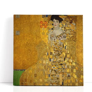 May include: A square canvas print of a Gustav Klimt painting. The artwork features a woman in a gold dress with intricate patterns, set against a gold background. The woman wears a black hat and a choker necklace.