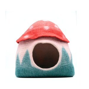 May include: A felt mushroom-shaped pet bed with a red top and white polka dots, a pink interior, and a teal green base with white accents.