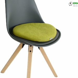 K&ouml;nnte beinhalten: Ein rundes, lindgr&uuml;nes Filz-Sitzkissen auf einem dunkelgrauen geformten Stuhl mit hellen Holzbeinen. Das Kissen hat ein kleines wei&szlig;es Etikett an der Seite. Das Logo von Woolly Felt The Felt Studio ist in der oberen rechten Ecke zu sehen.