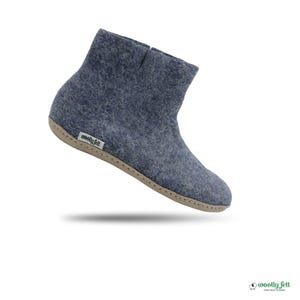 May include: A blue-grey felt ankle boot with a light beige sole and a small white tag on the side featuring the text woolly felt. The boot has a rounded toe, a high ankle collar, and visible stitching along the edge of the sole.