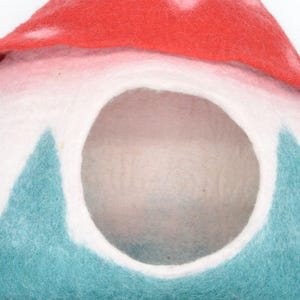May include: A felt pet bed shaped like a mushroom with a red top and a teal and white bottom. The bed has a large opening for a pet to enter.