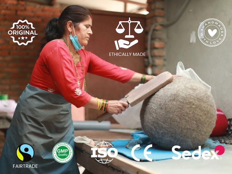 May include: A large, round, textured grey wool dryer ball being shaped with a wooden paddle. The image includes text overlays: 100% ORIGINAL, ETHICALLY MADE, HANDMADE WITH LOVE, FAIRTRADE, GMP Quality, ISO, CE, and Sedex, indicating quality standards.