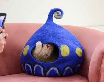 May include: A blue and yellow felt cat bed shaped like a spaceship with a cat peeking out of the entrance.