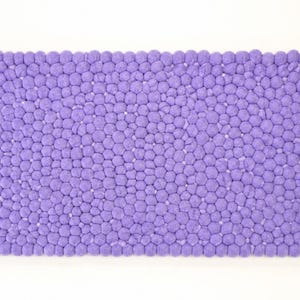 May include: A rectangular bath mat featuring a dense, textured surface composed of numerous small, uniform purple felted spheres arranged in a tight, honeycomb-like pattern. The mat has a consistent, vibrant purple colour throughout its entire structure.