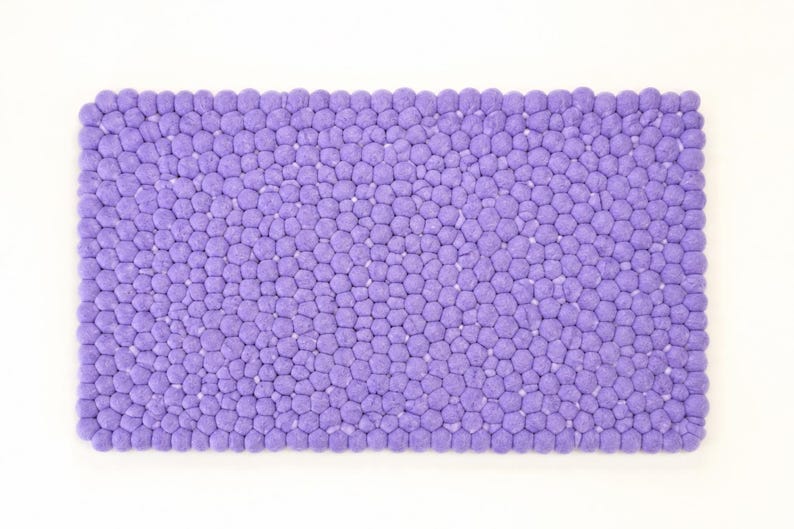 May include: A rectangular bath mat featuring a dense, textured surface composed of numerous small, uniform purple felted spheres arranged in a tight, honeycomb-like pattern. The mat has a consistent, vibrant purple colour throughout its entire structure.