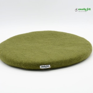 K&ouml;nnte beinhalten: Ein rundes, olivgr&uuml;nes Kissen aus gefilzter Wolle mit einer weichen, strukturierten Oberfl&auml;che. Ein kleines wei&szlig;es Stoffetikett mit dem schwarzen Text "woolly felt" ist am Rand befestigt. Das Logo "woolly felt THE FELT STUDIO" mit einem Schaf-Symbol ist dar&uuml;ber zu sehen.