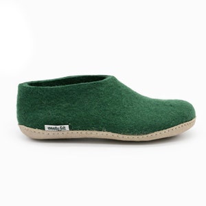 May include: Green wool felt slippers with a brown leather sole. The slippers have a simple design and are labeled "woolly felt" on the sole.