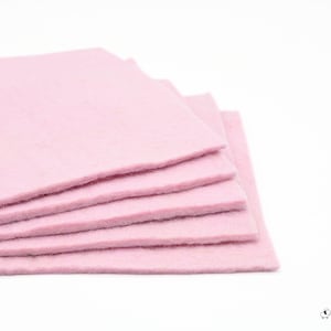 May include: A stack of six light pink felt squares, each with a slightly textured surface. The squares are neatly arranged, with the edges of each visible, creating a layered effect against a white background. The felt appears soft and pliable.