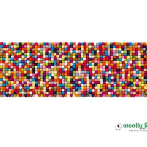 May include: A rectangular mat composed of numerous small, multi-coloured felt balls in shades of red, orange, yellow, green, blue, purple, and pink. The text "woolly felt THE FELT STUDIO" with a small sheep icon appears in the bottom right corner.