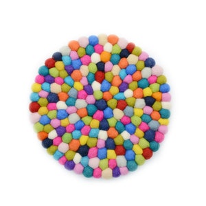 May include: A circular trivet constructed from numerous small, densely packed felt balls in a vibrant array of colours including red, orange, yellow, green, blue, purple, pink, and white, arranged in a concentric pattern on a white background.