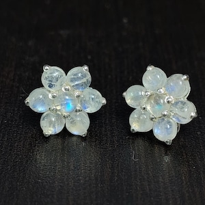 Könnte beinhalten: Ein Paar silberne Ohrringe in Blumenform mit weißen Mondstein-Edelsteinen.