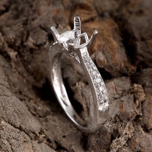 Op de afbeelding: Een zilveren ring met een kraalbezetting voor een middelste steen en een band met kleine diamanten.