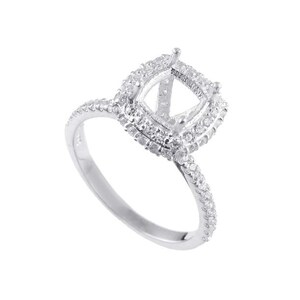 Könnte beinhalten: Ein silberner Ring mit einer Kissenform-Fassung, die von kleinen Diamanten umgeben ist. Die Ringschiene ist ebenfalls mit kleinen Diamanten besetzt.