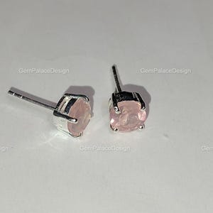 Könnte beinhalten: Ein Paar Ohrstecker mit runden, hellrosa Edelsteinen, die in silberfarbenem Metall gefasst sind. Die Ohrringe haben ein schlichtes, elegantes Design. Der Markenname "GemPalaceDesign" ist sichtbar.
