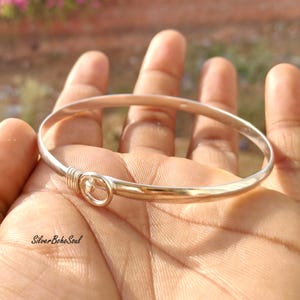 May include: A silver-toned bangle bracelet with a gold-colored accent. The bracelet features a simple, elegant design with a looped closure. The text "Silver Boho Soul" is visible in the image.