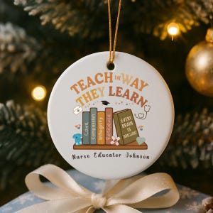 May include: A white ceramic ornament with the text "Teach the Way They Learn" in orange and brown. Below are illustrated books with words like "Care" and "Integrity." The ornament includes the name "Nurse Educator Johnson."