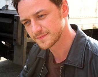 May include: A man with short brown hair and a beard is wearing a black leather jacket over a brown t-shirt with the text "Wonders" on it.